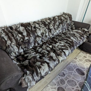 May include: A black leather couch with a silver fox fur throw draped over it. The couch is in a living room setting with a rug and a table.