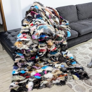 Puede incluir: Una manta de piel multicolor hecha de diferentes pieles de animales. La manta está drapeada sobre un sofá gris y un otomano de cuero negro.
