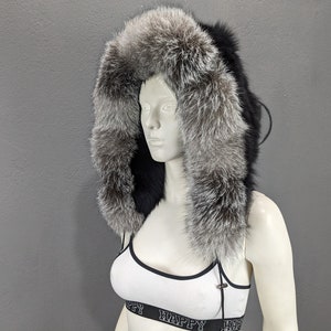 Puede incluir: Una chaqueta de piel negra con capucha y ribete de piel de zorro plateado. La capucha está forrada con piel de zorro plateado.