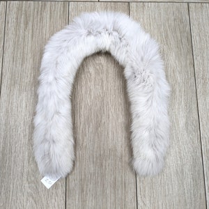 May include: A white faux fur collar for a jacket or coat. The collar is shaped like a U and is made of soft, fluffy fur.