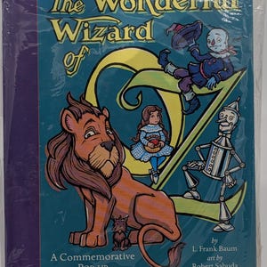 May include: A commemorative pop-up book titled "The Wonderful Wizard of Oz." The cover features illustrations of the Lion, Dorothy, the Scarecrow, the Tin Man, and the Wicked Witch. The book is by L. Frank Baum, with art by Robert Sabuda.