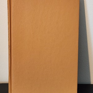 May include: A tan-colored hardcover book with a textured cover.