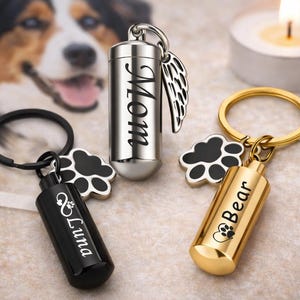 Puede incluir: Tres llaveros conmemorativos para mascotas. Uno es plateado con "Mom" grabado, otro es negro con "Luna" grabado y el tercero es dorado con "Bear" grabado. Cada llavero tiene un dije de huella de pata.