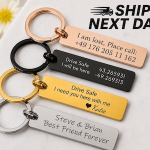 May include: Keychains with engraved rectangular tags in various colors: rose gold, black, gold, and silver. The tags have different messages, including contact information, GPS coordinates, and personal sentiments. Each keychain has a metal ring.
