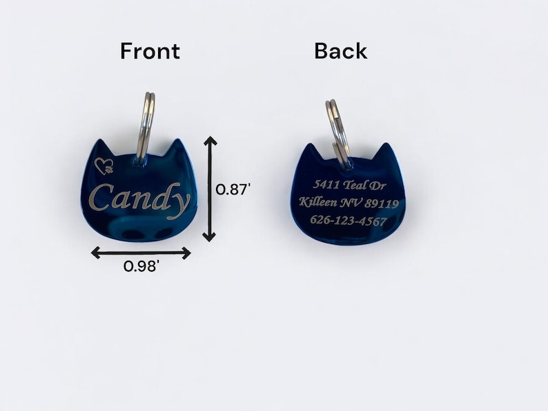 May include: A dark blue cat-shaped metal pet ID tag with a silver split ring. The front features the name Candy and a heart icon. The back displays the address 5411 Teal Dr, Killeen NV 89119 and phone number 626-123-4567. Dimensions are 0.98 inches by 0.87 inches.