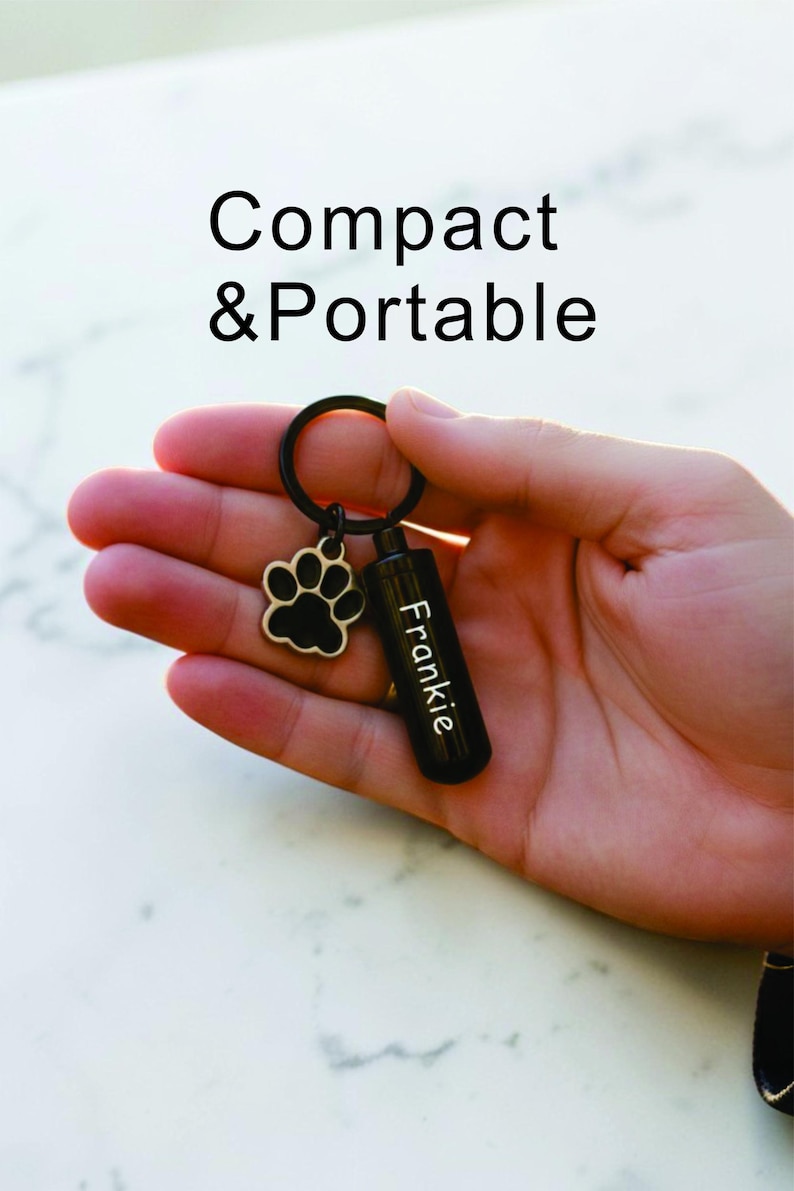 May include: Black keychain with a paw print charm and a small, black cylinder engraved with the name "Frankie." The text "Compact & Portable" is above the keychain. The keychain is held in a hand.