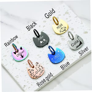 May include: Six cat-shaped pet ID tags in rainbow, black, gold, silver, blue, and rose gold finishes. Each tag features a metal jump ring and custom engraved names and graphics, including Oliver, Asher, Misha, Cola, Emily, and Cola with heart patterns.