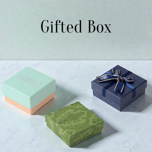 May include: Three gift boxes in different colors. A light blue and peach box, a green patterned box, and a navy blue box tied with a ribbon that says "Best Wishes". The words "Gifted Box" are at the top.