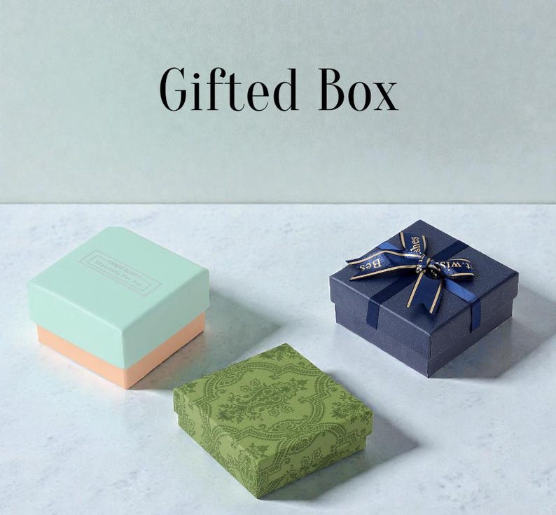 May include: Three gift boxes in different colors. A light blue and peach box, a green patterned box, and a navy blue box tied with a ribbon that says "Best Wishes". The words "Gifted Box" are at the top.