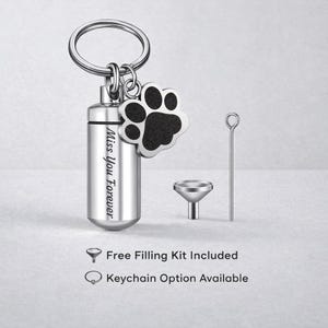 May include: A silver-colored pet urn keychain with a paw print charm. The urn is cylindrical and engraved with "Miss You Forever." A small funnel and filling tool are included. The keychain is designed for pet memorial keepsakes.