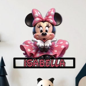 May include: A Minnie Mouse-themed wall decoration featuring a 3D figure with a pink polka-dot bow and dress. The name "ISABELLA" is displayed in pink glitter letters on a black rectangular plaque. A charming addition to a child's room.