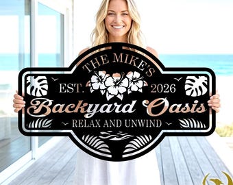 May include: Black metal sign with the text "THE MIKE'S Backyard Oasis" in a decorative font. The sign includes floral and leaf designs, the year "2026", and the phrase "RELAX AND UNWIND". The sign is held by a person.