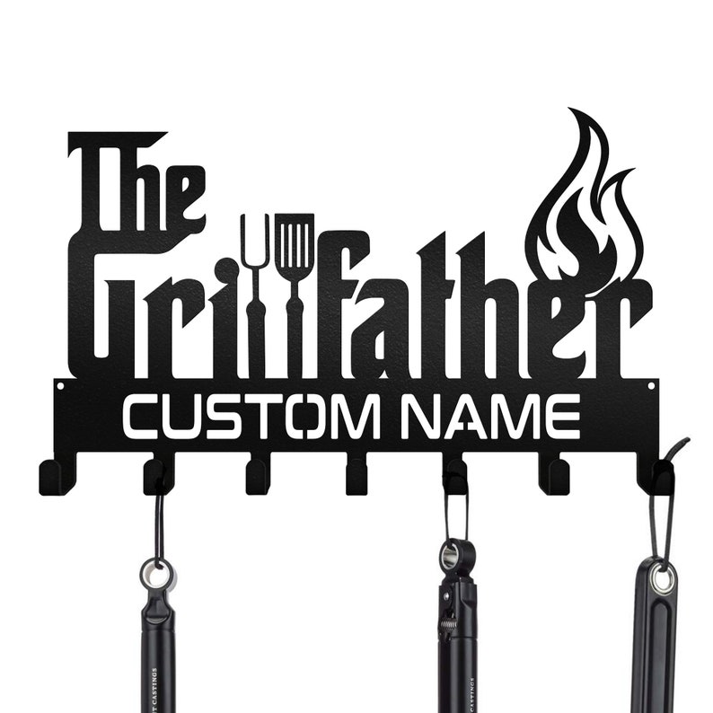 May include: Black metal wall-mounted hook rack with the text "The Grillfather" and a space for a custom name. The rack has six hooks and a flame design.