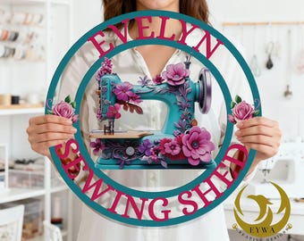 May include: A teal sewing machine with pink and purple floral accents is the centerpiece of a round sign. The sign has the text "EVELYN SEWING SHOP" in pink letters. The sign is held by a person.