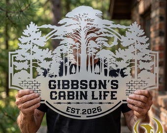 May include: A silver metal sign with a forest scene and the words "GIBBSON'S CABIN LIFE EST. 2026". The sign features a brick border and a barbed wire design.