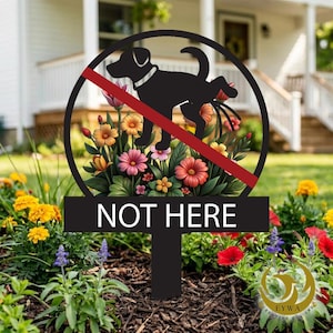Könnte beinhalten: Schwarzes Metall-Gartenschild mit einem kreisförmigen Design, das einen Hund zeigt, der auf Blumen uriniert, durchgestrichen mit einer roten Linie. Das Schild trägt die weiße Aufschrift "NOT HERE" und steht in einem Garten.