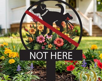 Op de afbeelding: Zwart metalen tuinbord met een cirkelvormig ontwerp met een silhouet van een hond die op bloemen plast, doorgestreept met een rode lijn. Het bord leest "NOT HERE" in witte letters en staat in een tuin.