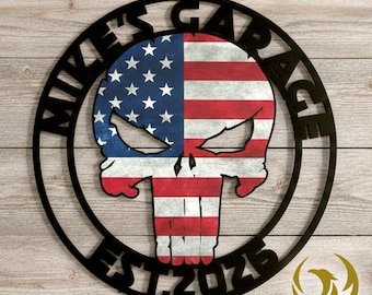 May include: Black metal garage sign featuring a skull design with the American flag incorporated into the skull's face. The sign is circular, with the words "MIKE'S GARAGE" and "EST 2025" in a bold font. A logo is in the bottom right corner.