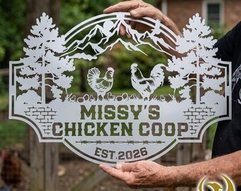 May include: A metal sign with the text "Missy's Chicken Coop" and "Est. 2026". The sign features a mountain range, two chickens, and trees. The sign is held up by a person.