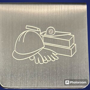 May include: A silver metal bookmark with a laser-etched design of construction tools, including a hard hat, gloves, bricks, and a level.