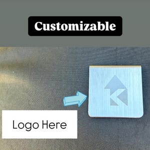 Op de afbeelding: Een zilveren metalen plaquette met een aanpasbaar logogebied. De plaquette heeft een geborstelde afwerking en een verhoogde rand. De tekst "Customizable" is in zwart op een witte achtergrond boven de plaquette gedrukt.