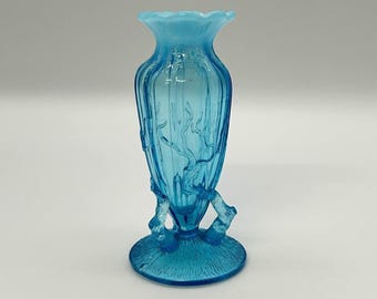 May include: A light blue glass vase with a flared rim and a textured base. The vase has a slender, elongated shape with vertical ribbing and decorative branch-like accents. The vase is approximately 6 inches tall.