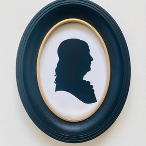 May include: A black silhouette of a person's head and shoulders in a gold and black oval frame. The text "Franklin" is written below the frame.