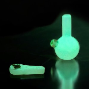 May include: A green glass bong with a round base and a small bowl. The bong is glowing in the dark.