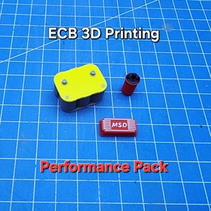 May include: A 3D printed performance pack for a car, featuring a yellow battery, a red MSD ignition box, and a black air filter. The text "ECB 3D Printing" and "Performance Pack" are visible in the image.