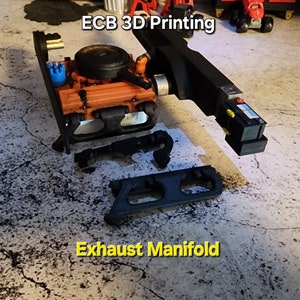 Peut inclure: Modèle d'un bloc moteur et d'un collecteur d'échappement imprimé en 3D. Le bloc moteur est orange et noir, et le collecteur d'échappement est noir. Le texte "ECB 3D Printing" est visible sur l'image.