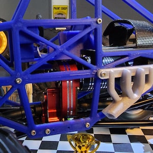 May include: A blue and gray model car with a detailed engine and exhaust system. The car has large tires and a roll cage. The car is sitting on a checkered floor.