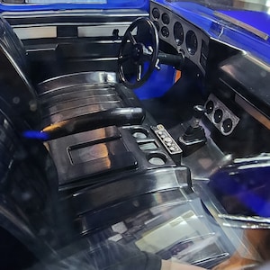 Puede incluir: El interior de un coche azul con asientos de cuero negro, un volante negro y un salpicadero negro. El coche tiene una consola central negra con una palanca de cambios y algunos botones.