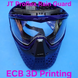 May include: A blue and black paintball mask with a clear lens. The mask has the text "JT Proflex Rain Guard" and "ECB 3D Printing" printed on it. The mask is designed to protect the face and eyes during paintball games.