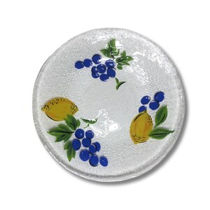 Può includere: Un piatto da portata in vetro bianco con una superficie testurizzata. Il piatto è decorato con un disegno dipinto di limoni e uva in tonalità di giallo, blu e verde.