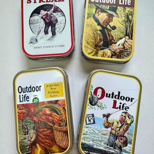 May include: Four vintage metal tins with images of men fishing. The tins are labeled "Field and Stream", "Outdoor Life", and "Outdoor Life".