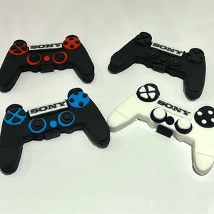 Puede incluir: Cuatro mandos de Playstation Sony de plástico de diferentes colores. Los mandos son negros, blancos, rojos y azules. Cada mando tiene la palabra "SONY" impresa.
