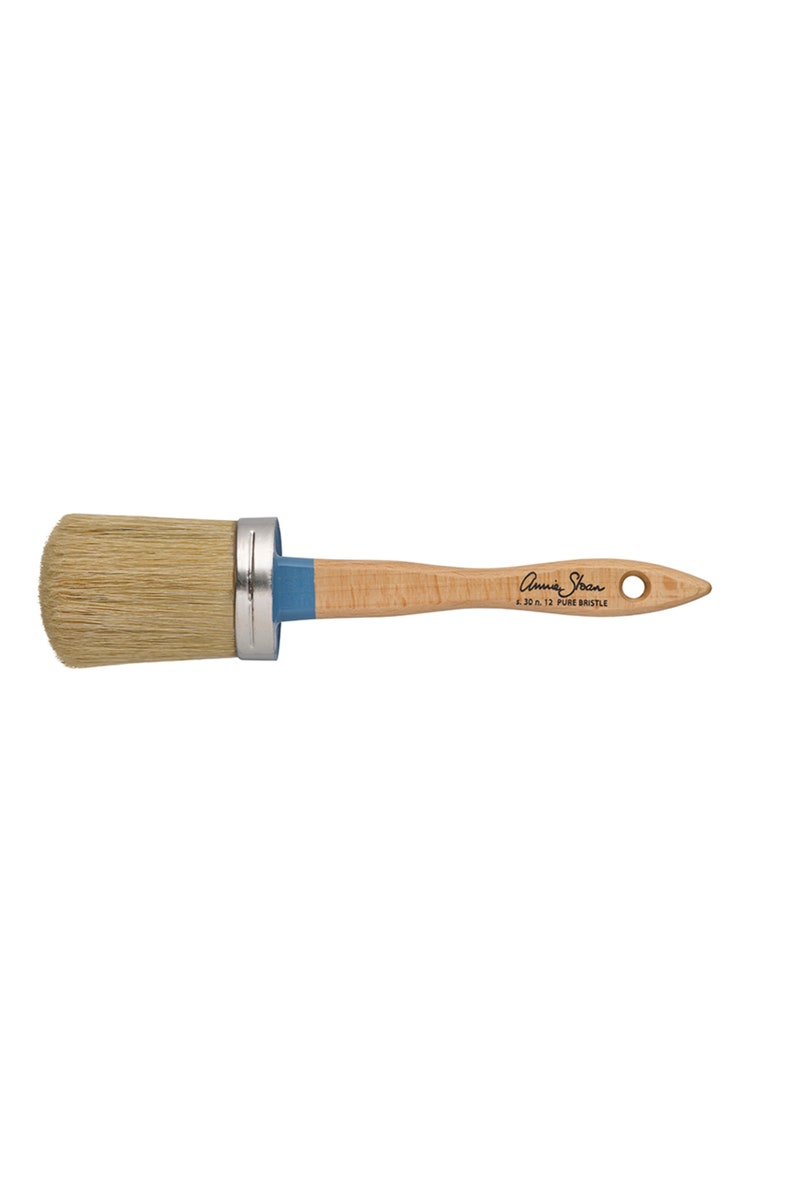 Puede incluir: Un pincel redondo de cerdas naturales con un mango de madera clara. El pincel tiene una virola de metal plateado y una secci&oacute;n azul donde el mango se encuentra con las cerdas. El texto "Annie Sloan" y "6.30 n. 12 PURE BRISTLE" est&aacute;n impresos en el mango.