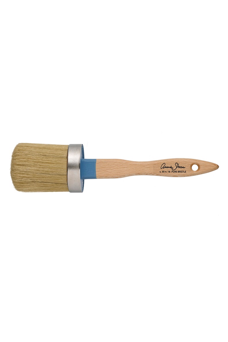Puede incluir: Un pincel redondo con cerdas naturales, un mango de madera y un acento azul. El pincel tiene una virola de metal y el texto "Annie Sloan" y "L. 30 n. 16 PURE BRISTLE" impreso en el mango.