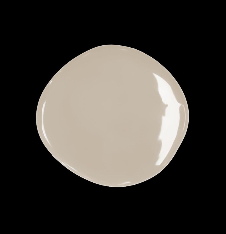 Puede incluir: Una muestra de pintura en forma de l&aacute;grima, de color beige claro y neutro. La pintura tiene un acabado brillante que refleja la luz. El fondo es negro, lo que resalta el color de la pintura.