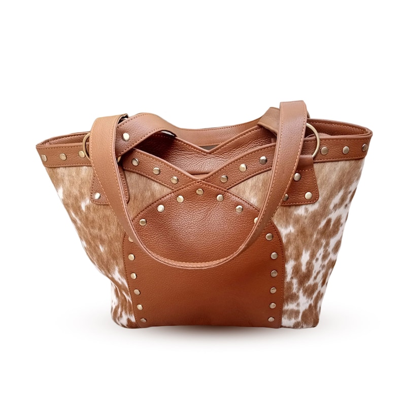 May include: A brown leather tote bag with a cowhide pattern and gold studs. The bag has two top handles and a zipper closure.