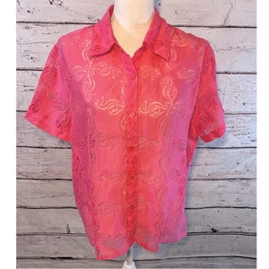 May include: A short-sleeved, button-down shirt in a vibrant pink hue. The shirt features an all-over floral pattern and a classic collar. The fabric appears to be semi-sheer, adding a delicate touch to the garment.
