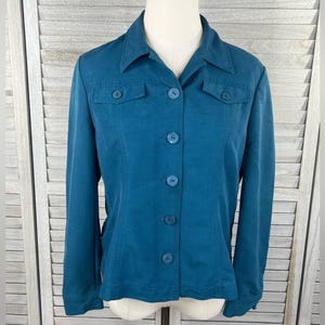 May include: Teal button-down jacket with two chest pockets and a collared neckline. The long-sleeved jacket has matching teal buttons and is displayed on a mannequin. The jacket is a solid color and appears to be made of a soft material.