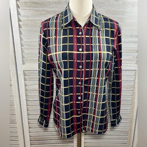 May include: A long-sleeved button-down shirt with a plaid pattern. The shirt features a navy blue base with a grid of red, yellow, and white lines. The shirt has a classic collar and buttoned cuffs.