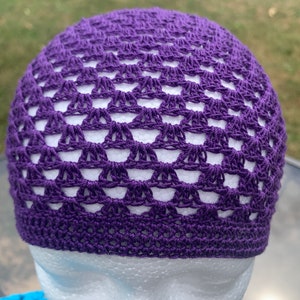 May include: Purple crocheted beanie hat with a lacy pattern. The hat is on a white mannequin head.