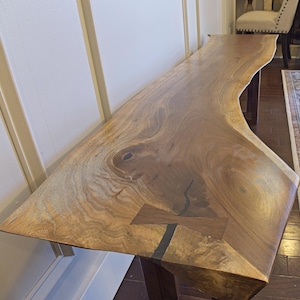 May include: A live edge wooden console table with a natural, organic shape. The table is made of light brown wood with a visible grain pattern and measures approximately 72 inches long.