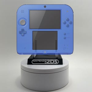 Peut inclure: Une console de jeu portable Nintendo 2DS bleue sur un présentoir rotatif blanc. La console comprend deux écrans, un pavé directionnel et des boutons. Le présentoir affiche le logo Nintendo 2DS.