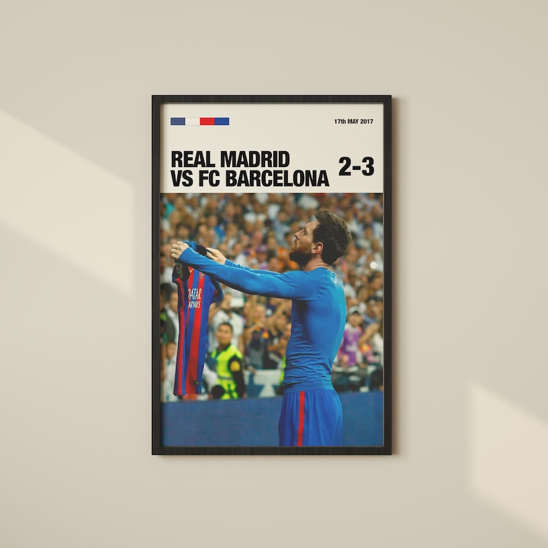 May include: Framed poster featuring a soccer player holding up a jersey. The poster includes the text "REAL MADRID VS FC BARCELONA 2-3" and the date "17th MAY 2017". The jersey is red and blue.