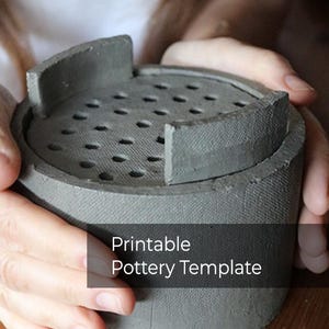 Könnte beinhalten: Eine graue, zylindrische Töpfereischablone mit perforierter Oberseite und zwei erhöhten rechteckigen Abschnitten. Der Text "Printable Pottery Template" ist auf der Vorderseite zu sehen. Die Schablone wird von zwei Händen gehalten.