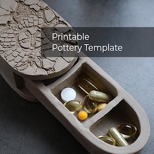Puede incluir: Un pastillero de cerámica abierto hecho a mano con tapa, que contiene varias pastillas y cápsulas. La tapa presenta un diseño floral texturizado. El texto "Printable Pottery Template" se muestra en la imagen.