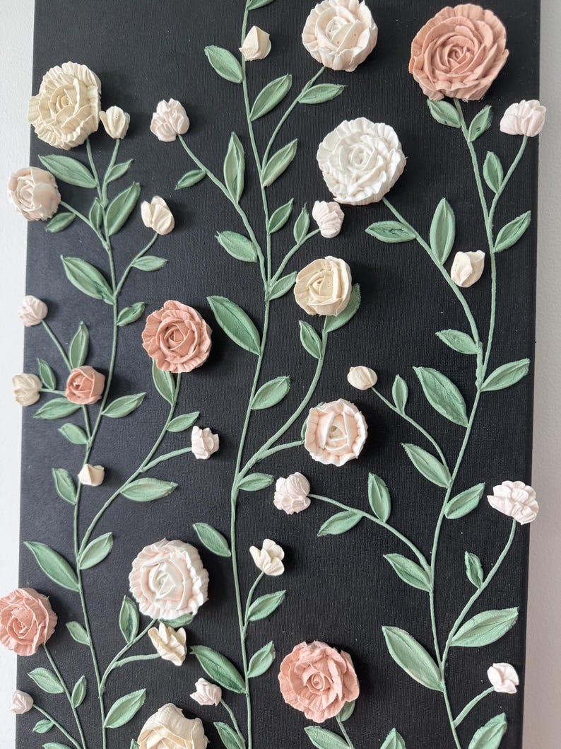 May include: A floral canvas artwork with textured roses in cream and peach hues, set against a black backdrop. The green leaves and stems add contrast. The raised design gives a three-dimensional effect, creating a tactile and visually appealing piece.